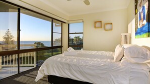 A bedroom with a large window offering a view of the ocean. There are two framed pictures on the wall and a painting on the right side.