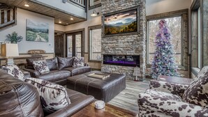 A spacious living room with a stone fireplace, leather sofas, and a Christmas tree. - Topside Splash | Pool, Hot Tub & Mountain Views (Gatlinburg)