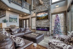 A spacious living room with a stone fireplace, leather sofas, and a Christmas tree.
