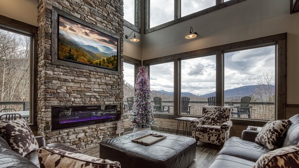 A spacious living room with a stone fireplace, leather furniture, a Christmas tree, and large windows offering mountain views. - Topside Splash | Pool, Hot Tub & Mountain Views (Gatlinburg)