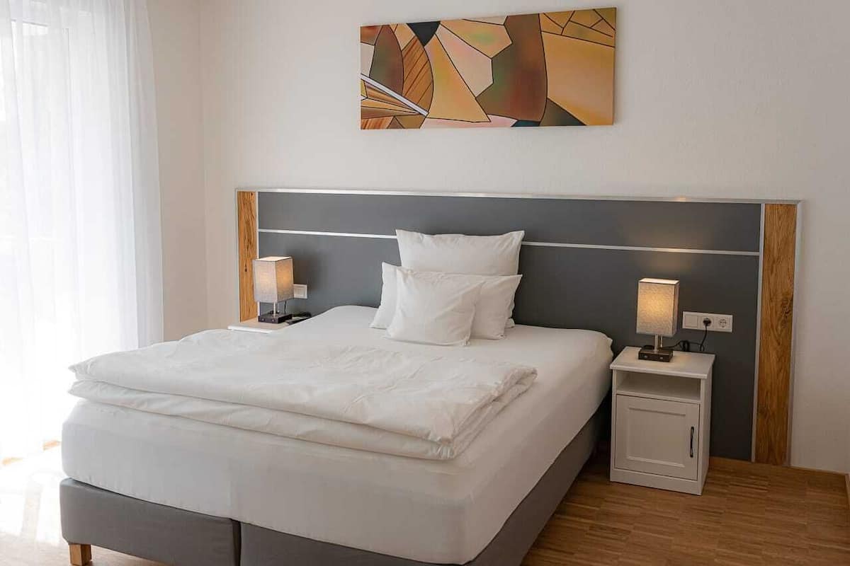 Un lit bien fait, avec du linge de lit blanc, une tête de lit moderne et des lampes de chevet de chaque côté.