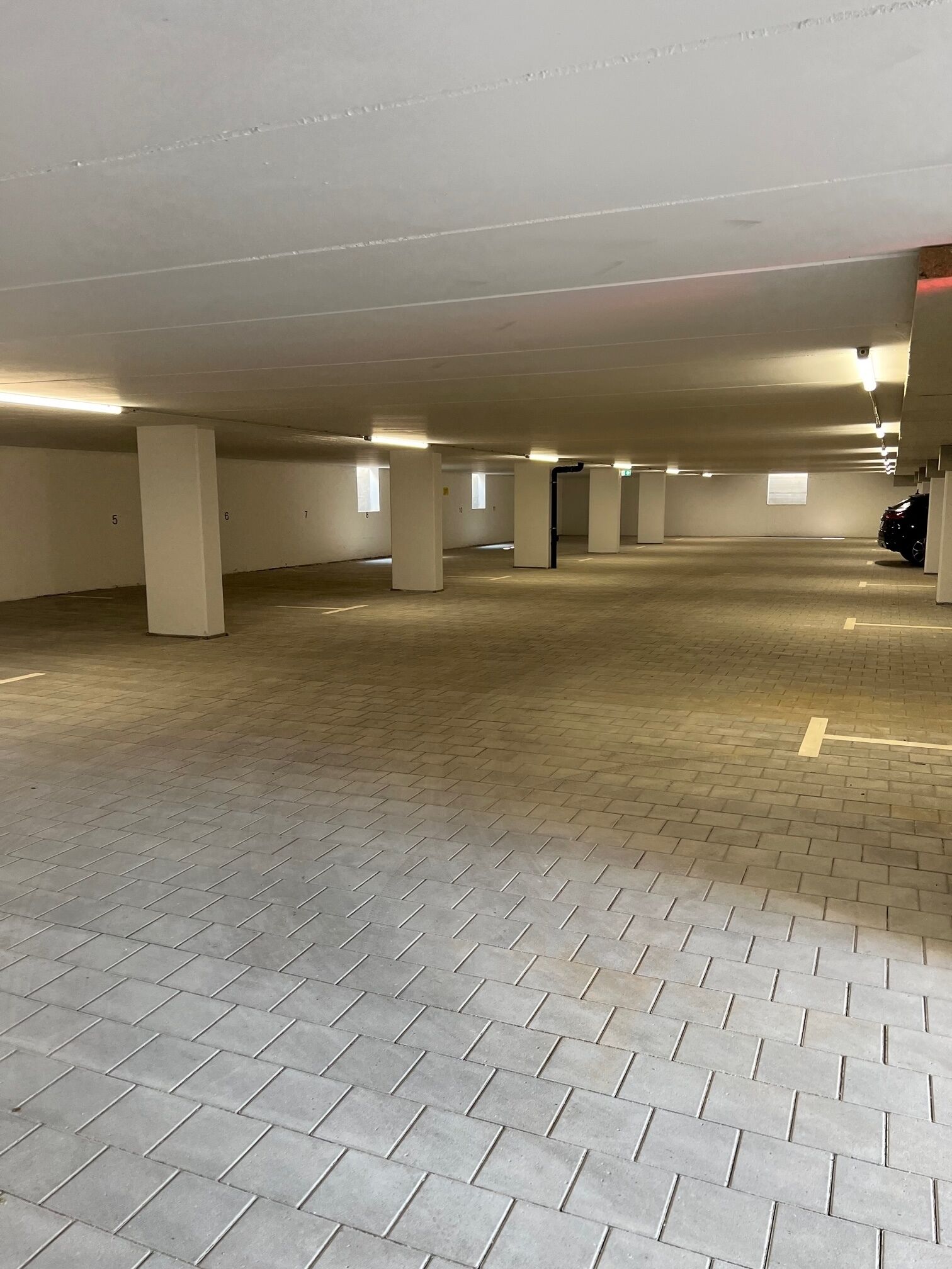 A spacious parking garage with concrete pillars and a tiled floor.