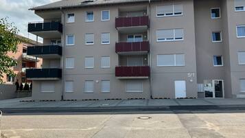 Un edificio residencial de varios pisos con balcones, una entrada a nivel de calle y un número de puerta visible.
