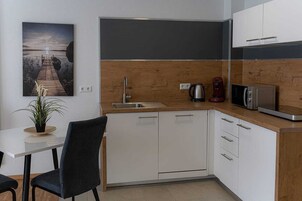 A modern kitchen with white cabinets, a wooden countertop, a sink, a coffee maker, and a microwave.