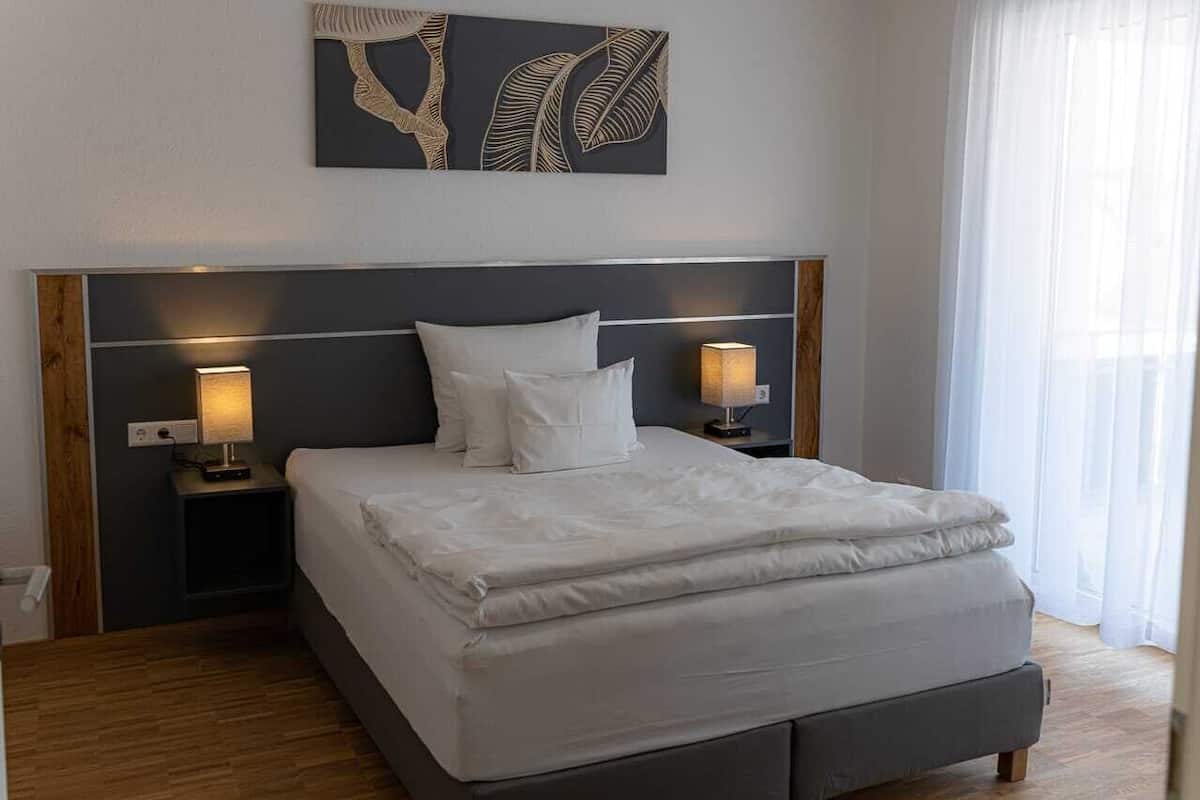 Un lit bien fait, avec du linge de lit blanc, deux lampes de chevet et une tête de lit moderne.