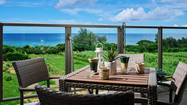 Un balcón con mobiliario de mimbre, una mesa con bebidas y vistas al océano y la vegetación.
