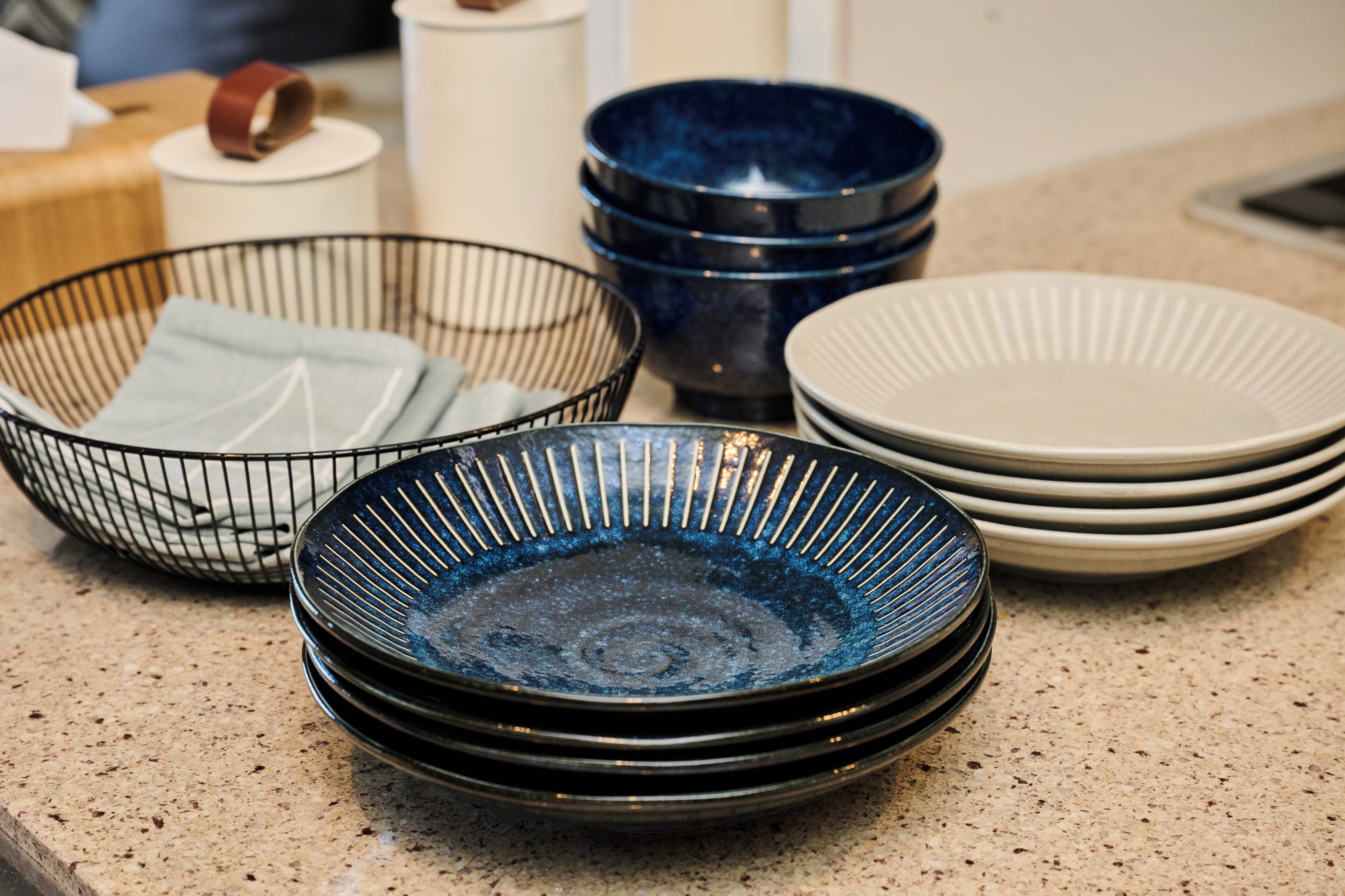 Un plan de travail de cuisine avec une pile d’assiettes, des bols et un panier en fil de fer.