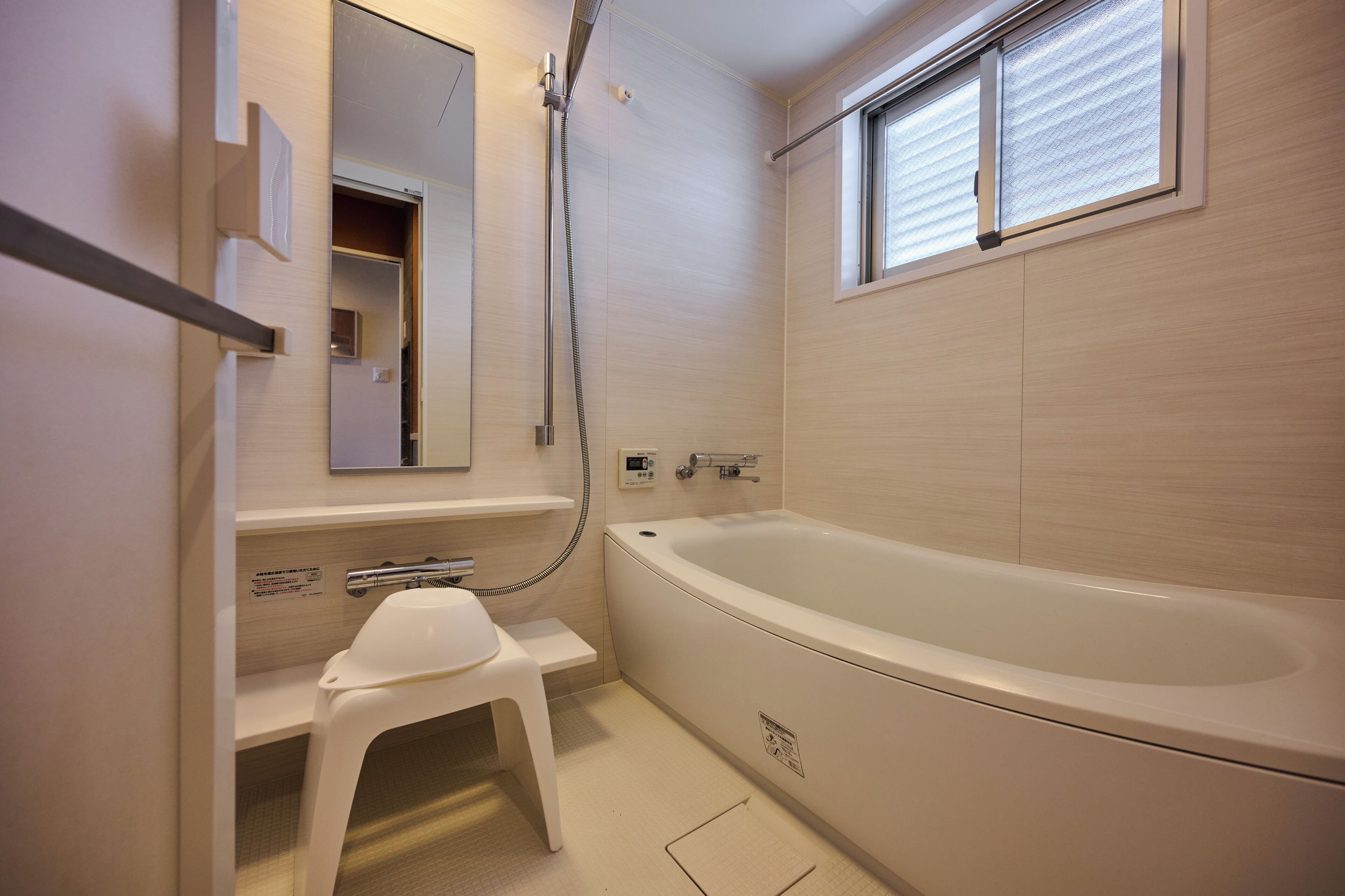 A modern bathroom with a large bathtub, a showerhead, and a small stool.