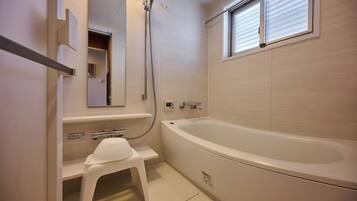 A modern bathroom with a large bathtub, a showerhead, and a small stool.