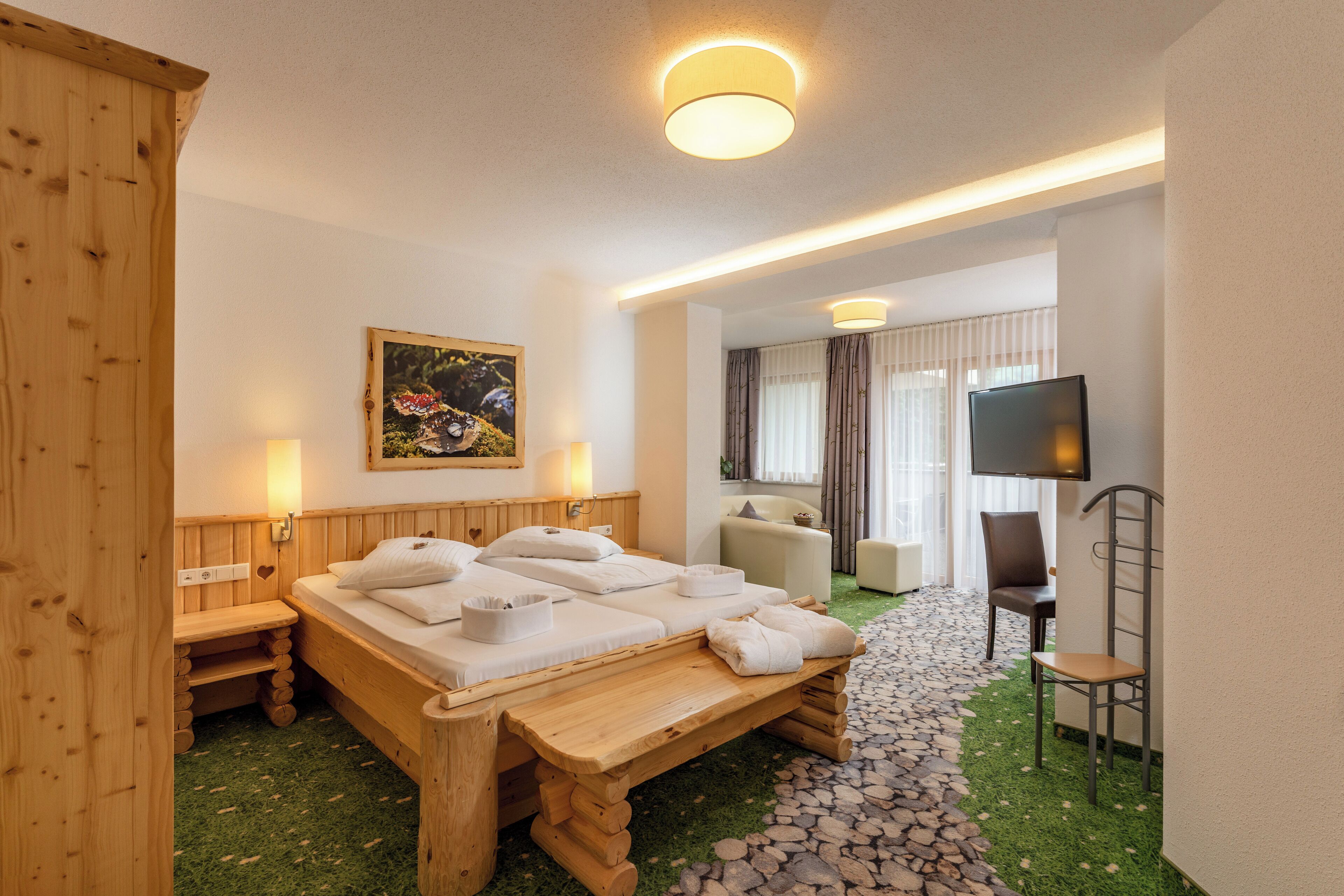Uma cama de madeira com almofadas e toalhas, uma televisão, uma cadeira e um quadro na parede.