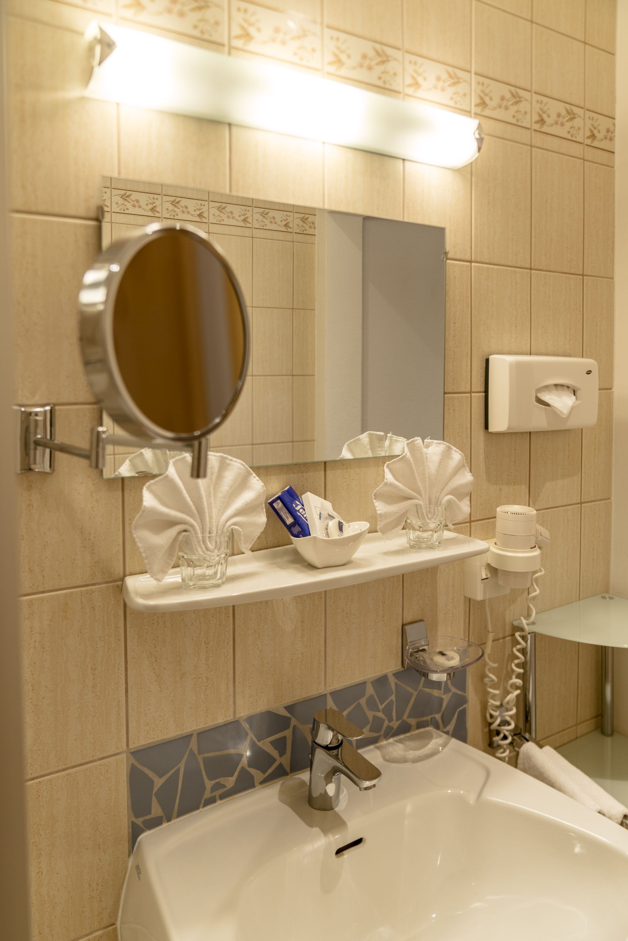 A bathroom with a sink, mirror, towel dispenser, and a tissue box.