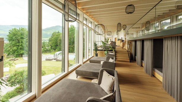 Un interior moderno con ventanas amplias, techo de madera y una zona de estar con cojines.