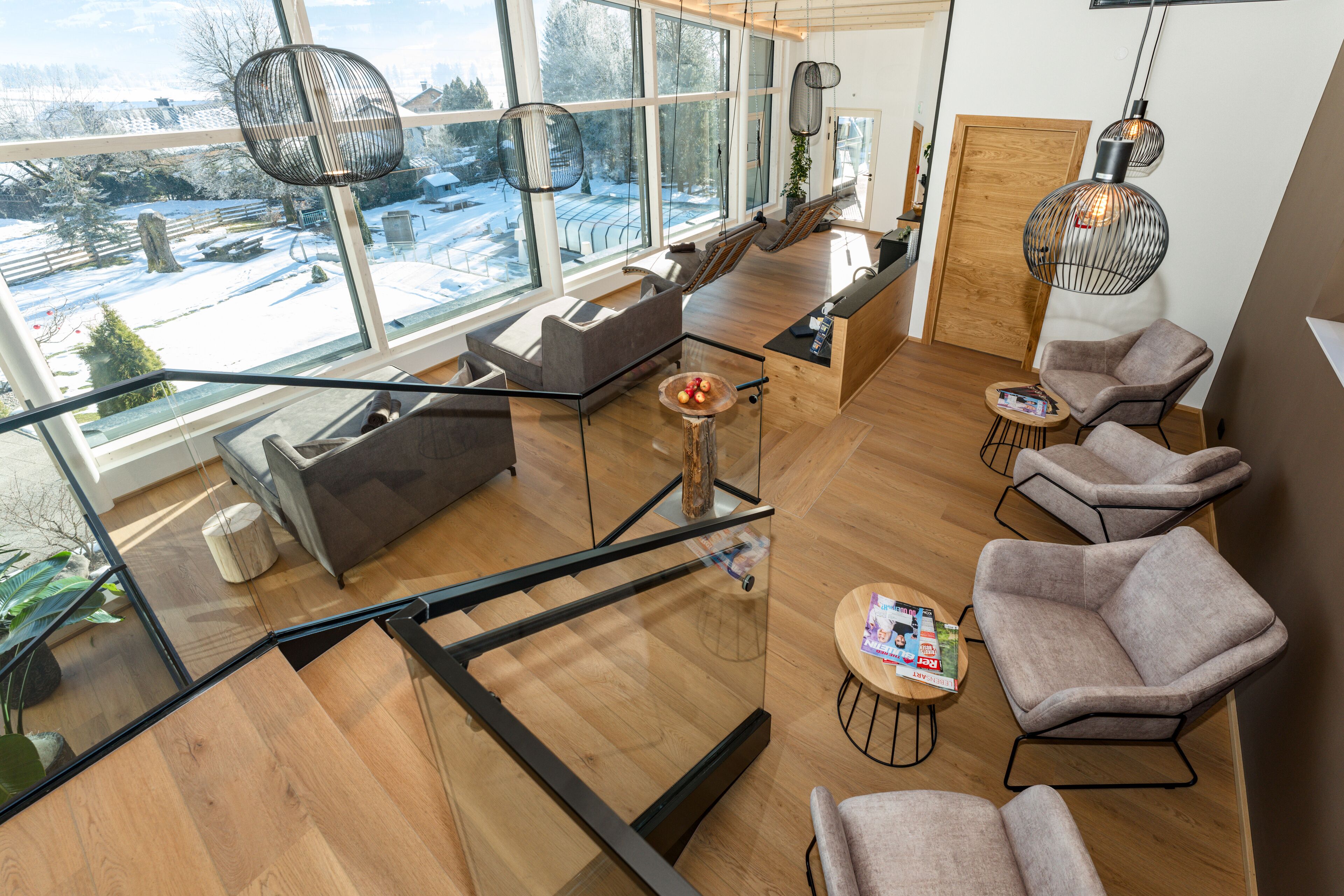 A modern interior with a glass staircase, seating area, and large windows offering a view of a snowy landscape.