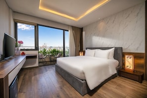 A modern hotel room with a large bed, a TV, a desk, and a balcony with a view of the city. - Luxury Duplex Penthouse With Pool Foosball (Da Nang)