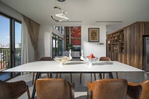 A modern dining area with a white table, brown leather chairs, and decorative vases. - Luxury Duplex Penthouse With Pool Foosball (Da Nang)
