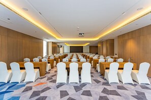A conference room with rows of tables and chairs, a projector screen, and a carpeted floor.