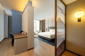 A modern hotel room with a desk, a bed, and a large window.