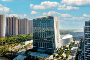 A modern hotel with a glass facade, surrounded by high-rise buildings and a landscaped area. - Holiday Inn Express Suzhou Bay (Suzhou)