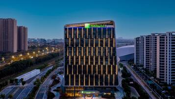 Un hotel moderno con un llamativo letrero de Holiday Inn Express, rodeado de edificios altos y un área de estacionamiento bien iluminada.