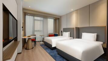 A hotel room with two beds, a TV, a dining table, and a window with curtains.