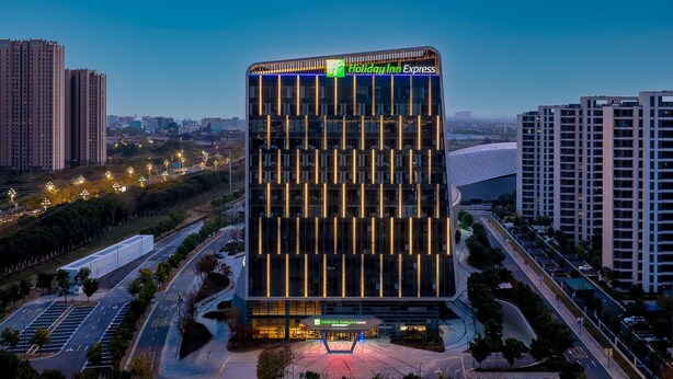 A modern hotel with a prominent Holiday Inn Express sign, surrounded by high-rise buildings and a well-lit parking area. - Holiday Inn Express Suzhou Bay (Suzhou)