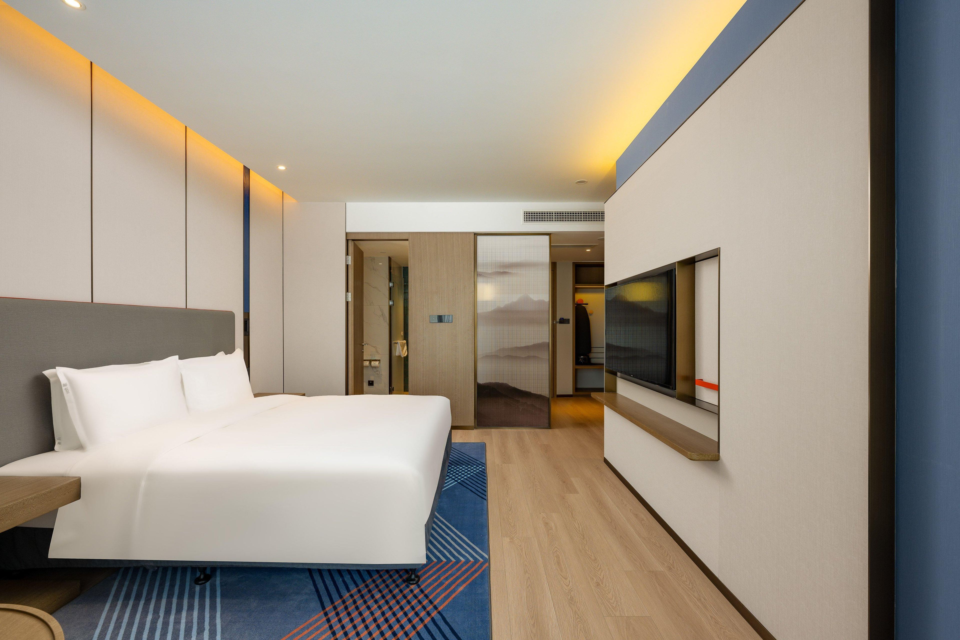 Quarto de hotel moderno com uma cama grande, televisão de tela plana e piso de madeira.