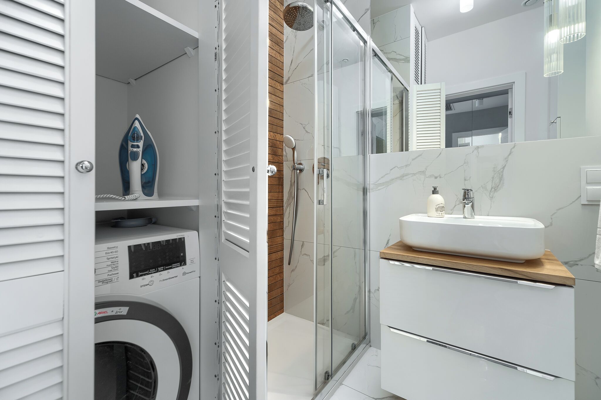 A modern bathroom with a glass-enclosed shower, a built-in washing machine, and a vanity with a marble countertop.