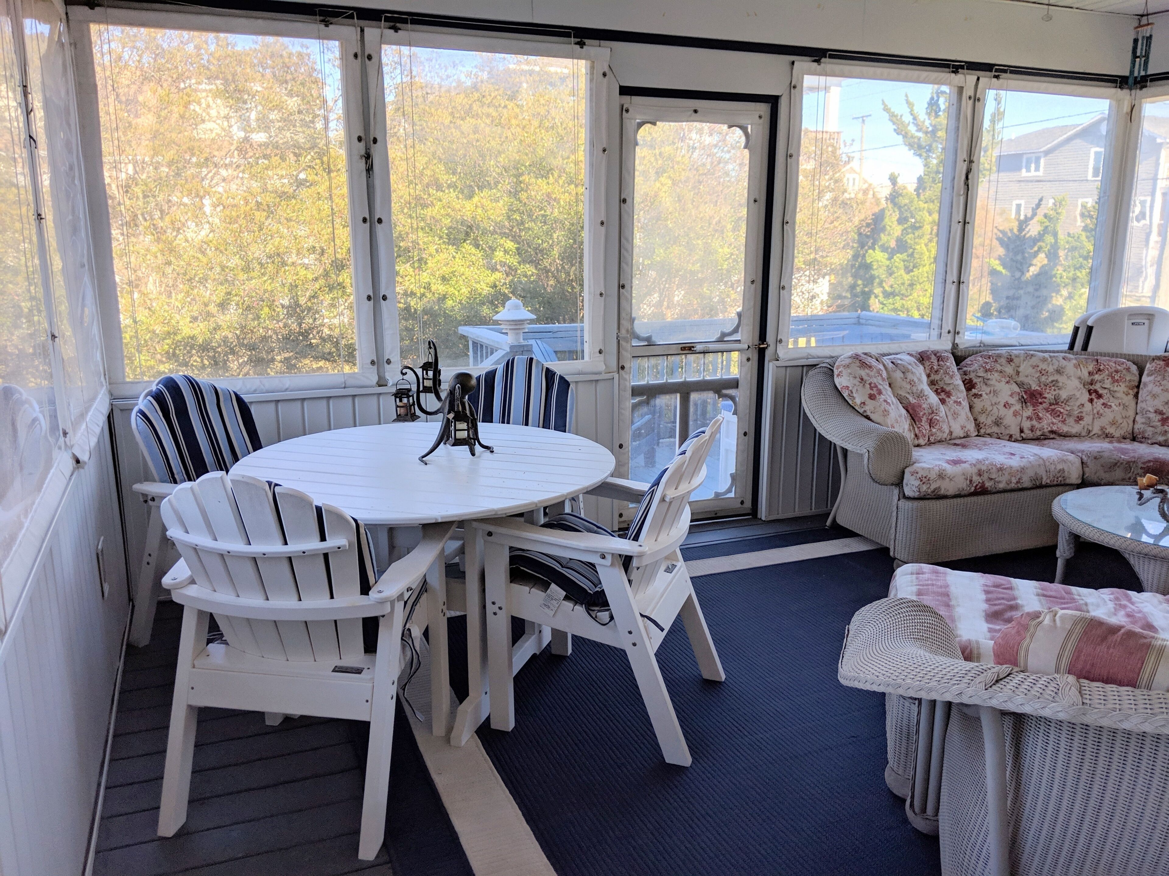 A covered outdoor seating area with a round table and chairs, a sofa, and a wicker chair.