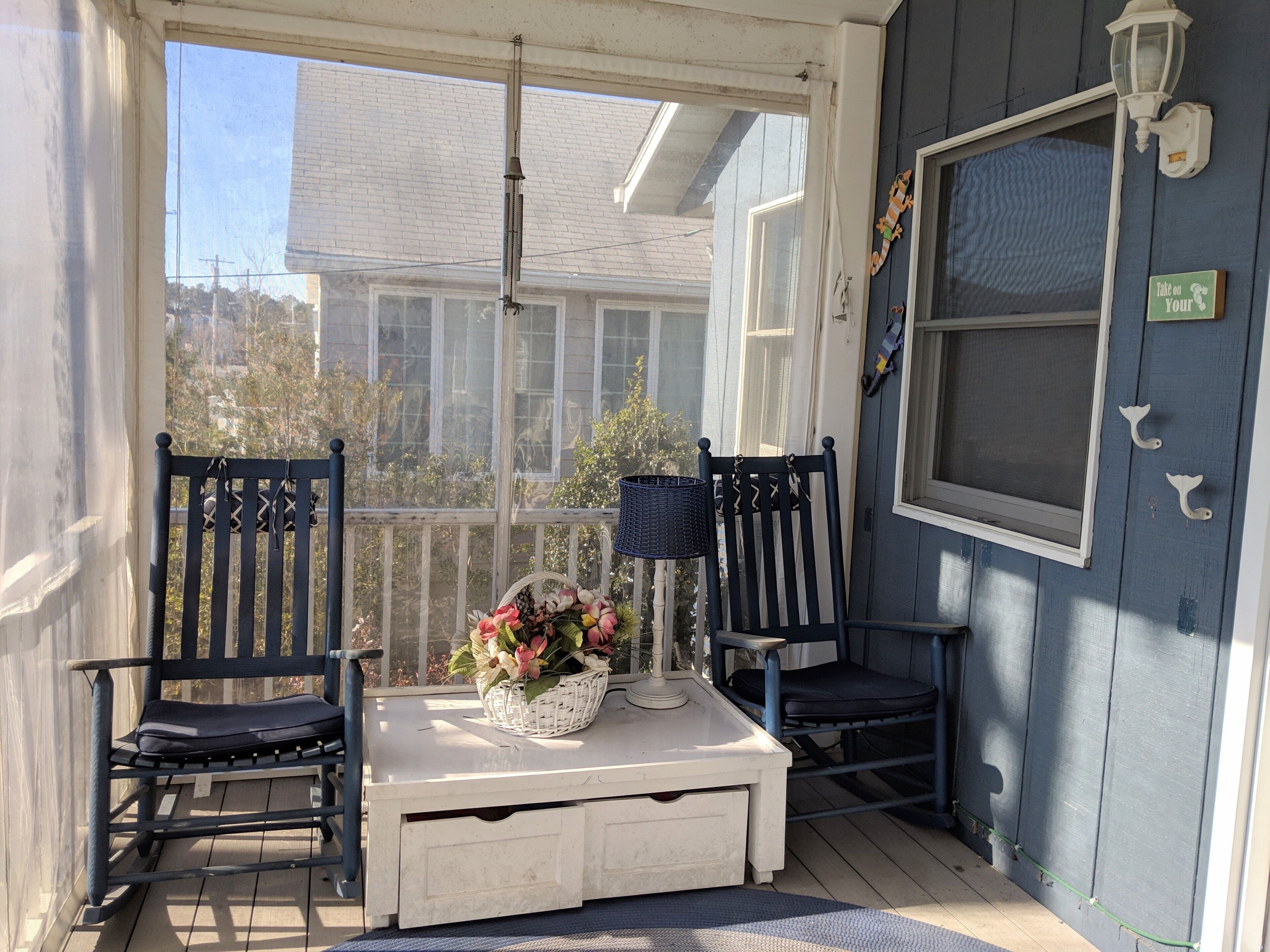 Eine überdachte Veranda mit zwei Stühlen, einem Tisch mit einem Blumenkorb und einer Wandleuchte.