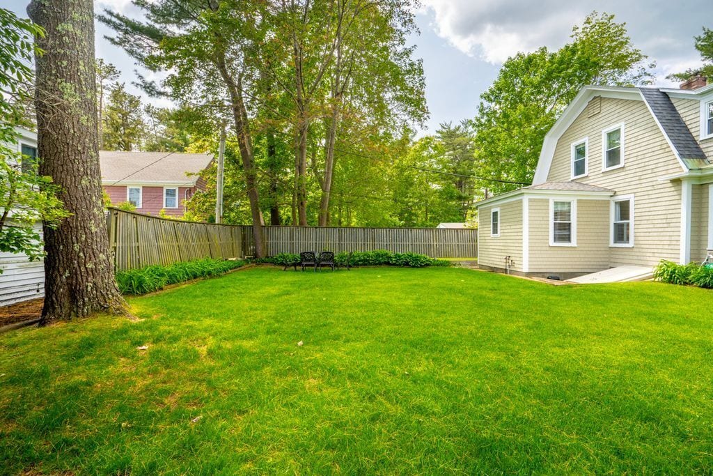 A backyard with a wooden fence, a tree, and a house.