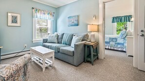 A cozy room with a gray sofa, a small white table, and a bed with a blue and white quilt. - Beautiful inn, Lighthouse Landing. #3 Sea Glass (Ogunquit)