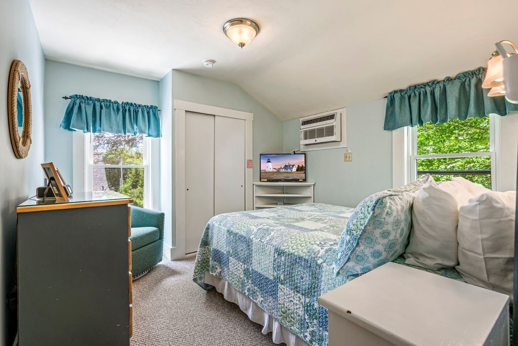 Une chambre à coucher avec un lit, une commode, un téléviseur et une fenêtre avec des rideaux.