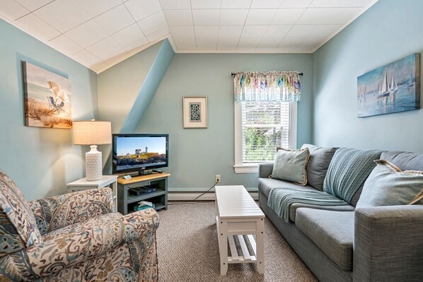 A living room with a television, patterned sofa, and a window with curtains. - Beautiful inn, Lighthouse Landing. #3 Sea Glass (Ogunquit)