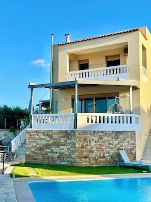 A two-story building with a pool, stone facade, and a balcony with a white railing. - Villa Cook with pool and sea views (Platanias)