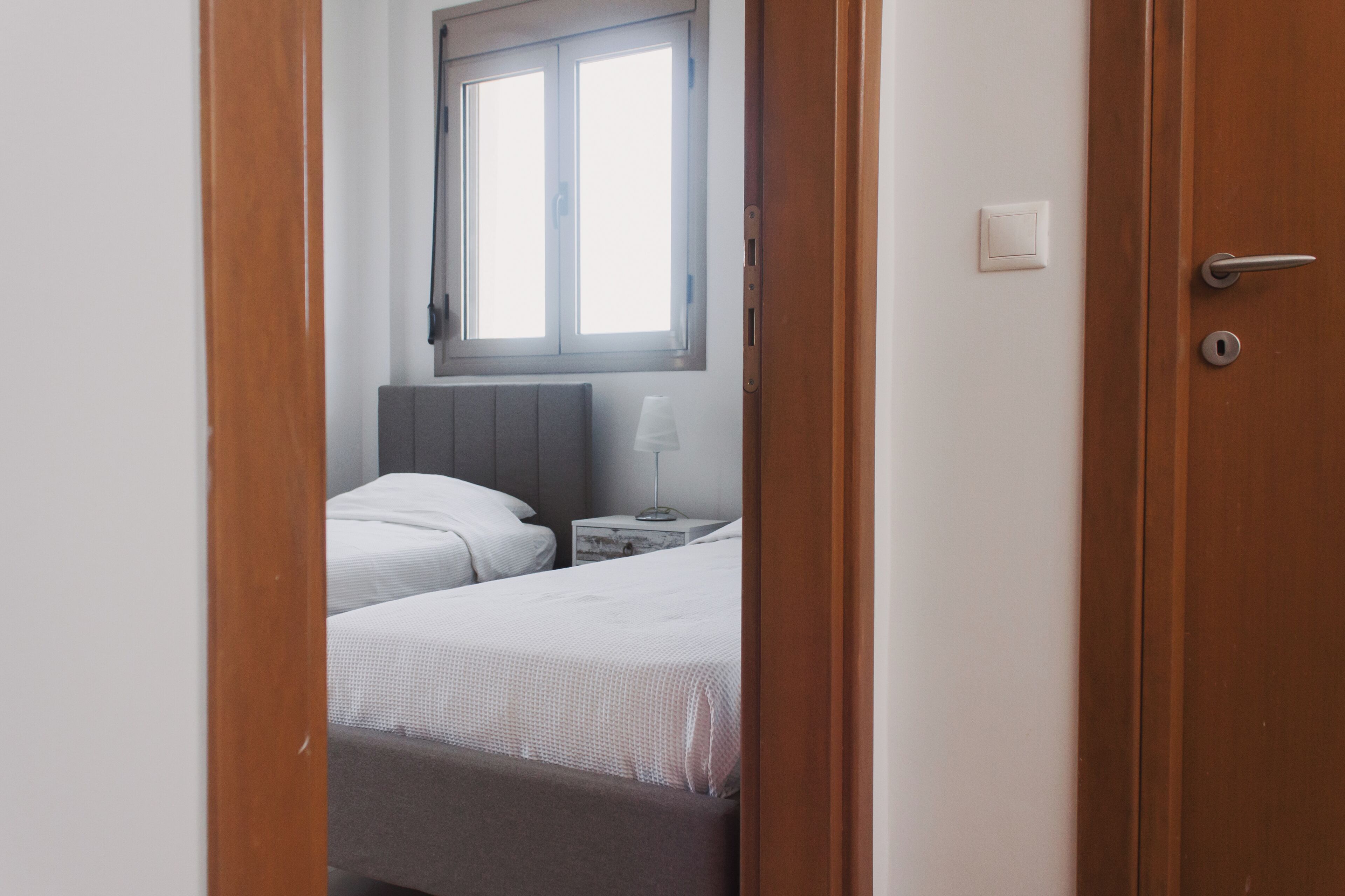 A hotel room with a bed, bedside table, lamp, and window.