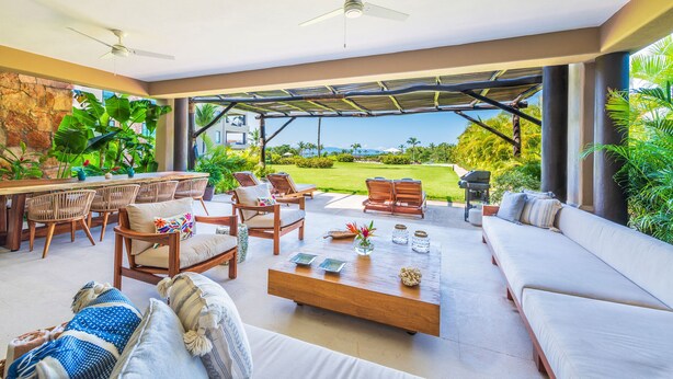A spacious outdoor patio with a dining area, seating, and a view of the landscape. - Luxurious 4 Bedroom Condo (Punta de Mita)