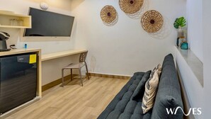 Una sala de estar moderna con un sofá, un televisor montado en la pared y un escritorio pequeño con una silla.