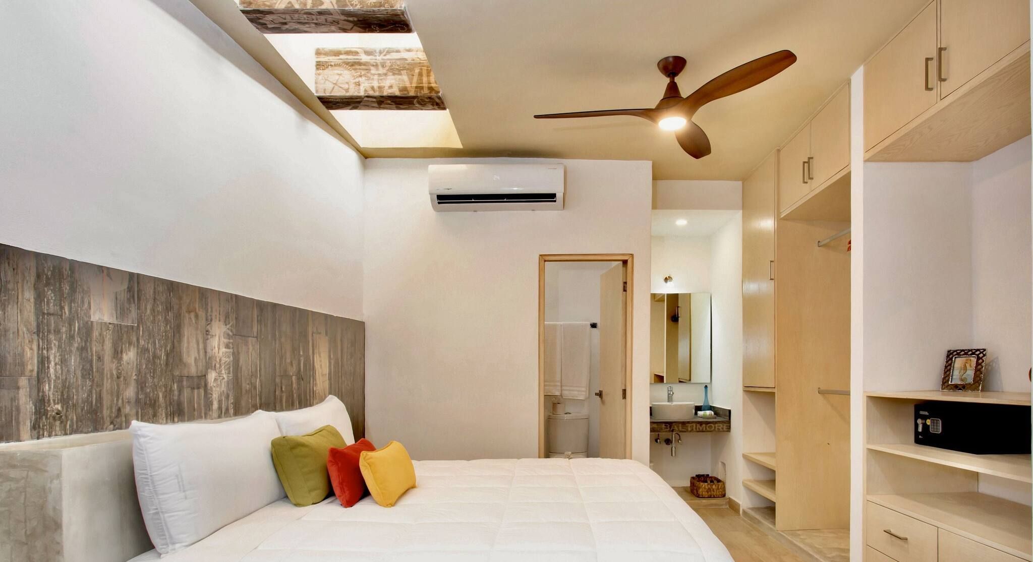 A bedroom with a bed, pillows, an air conditioning unit, a ceiling fan, and a skylight.