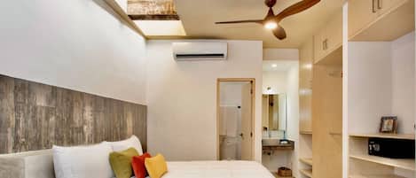 A bedroom with a bed, pillows, an air conditioning unit, a ceiling fan, and a skylight.