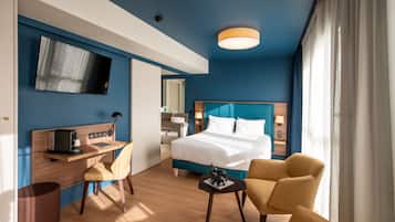 A modern hotel room with a large bed, a desk with a computer, a chair, and a small table with a decorative item.