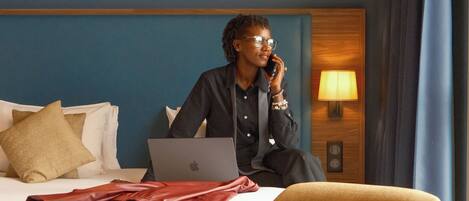 A hotel room with a bed, a laptop, a red handbag, and a lamp.