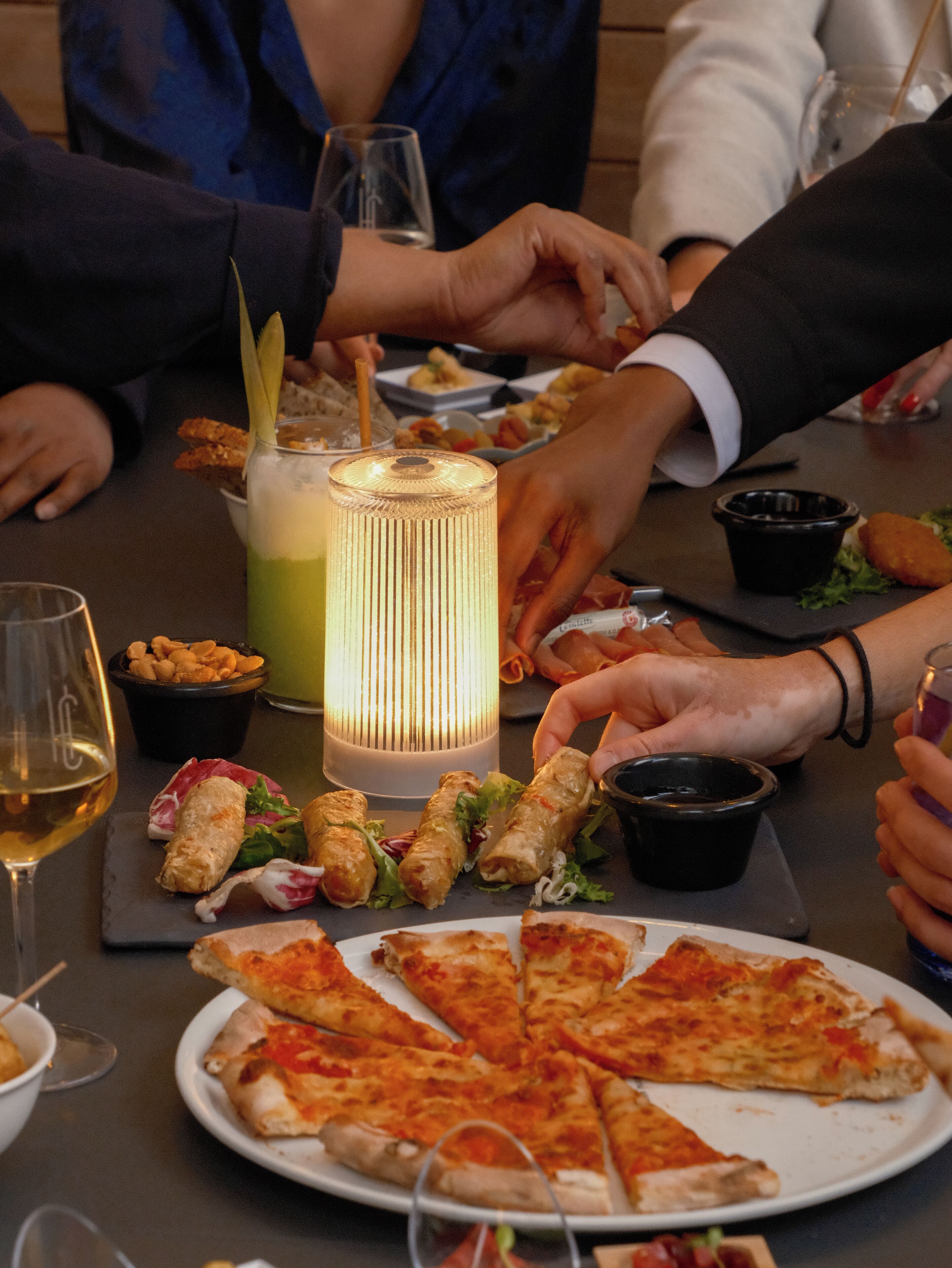 Una mesa de comedor con porciones de pizza, un cóctel y aperitivos.