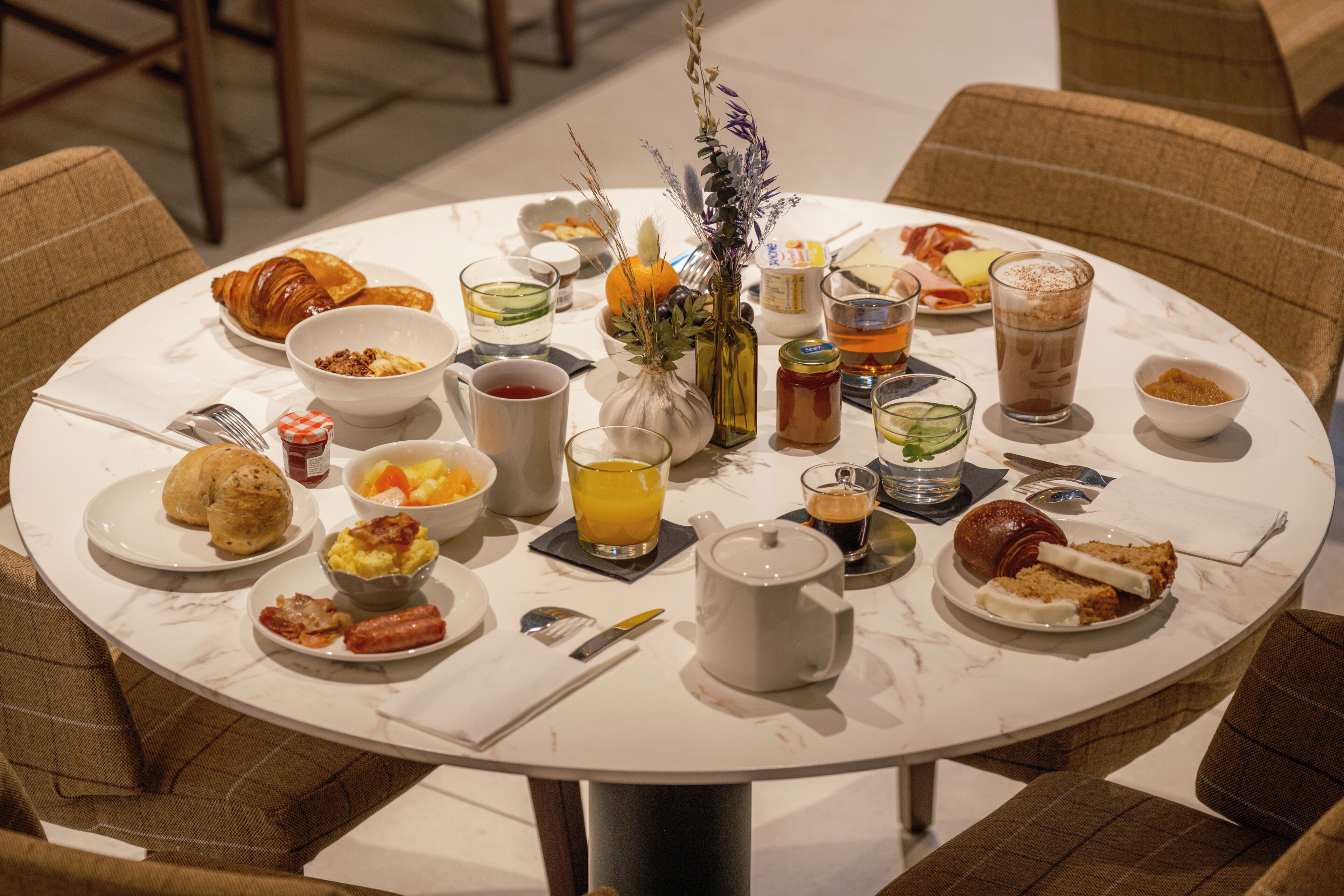 Una mesa redonda para comer con diversos alimentos de desayuno, como cruasanes, huevos y bebidas.