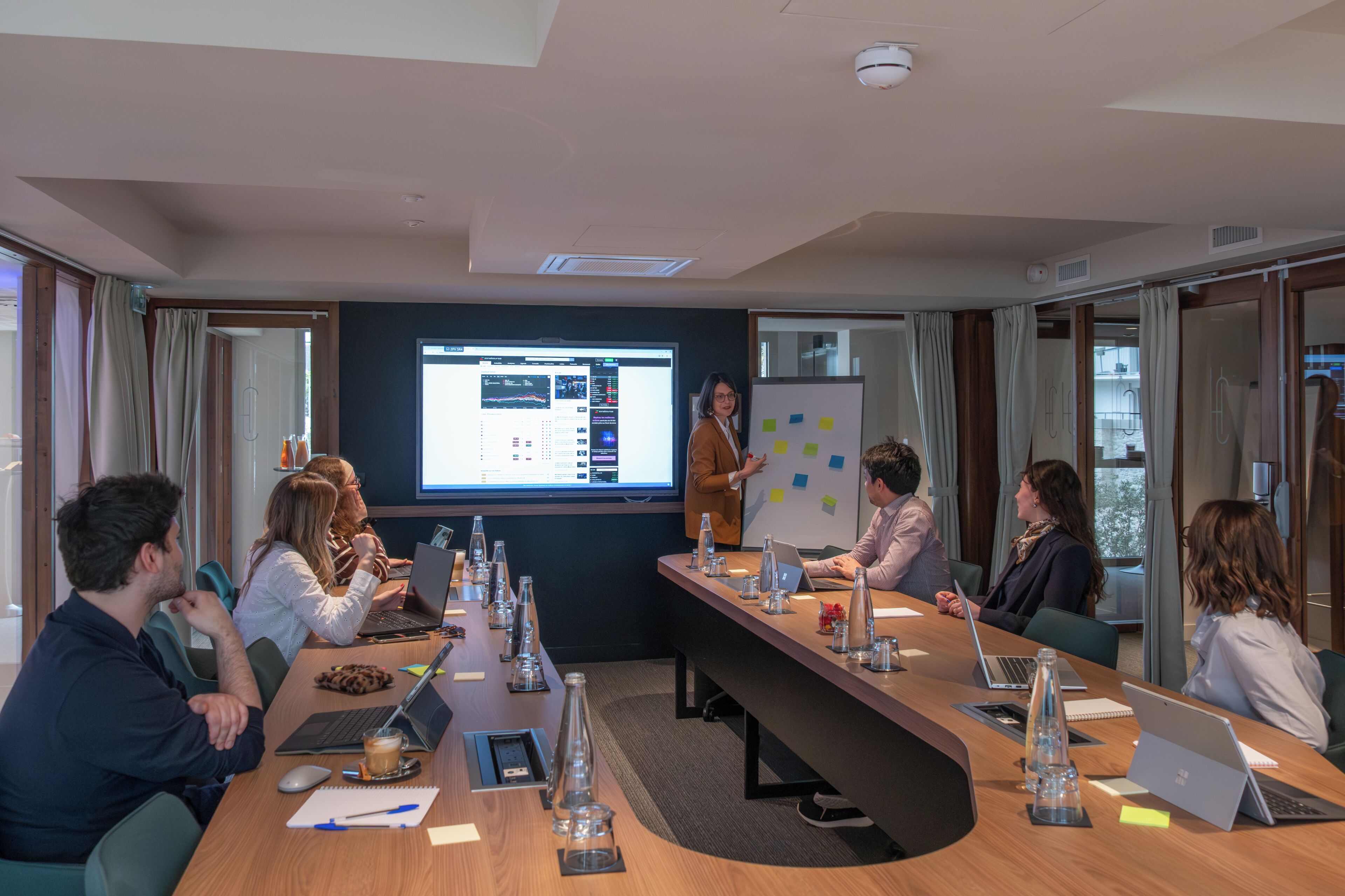 Een vergaderzaal met een presentatiescherm, een whiteboard en een lange tafel met laptops en waterflessen.
