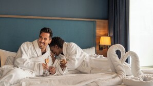 Una habitación de hotel con una cama, una mesita de noche con lámpara y una ventana con cortinas.