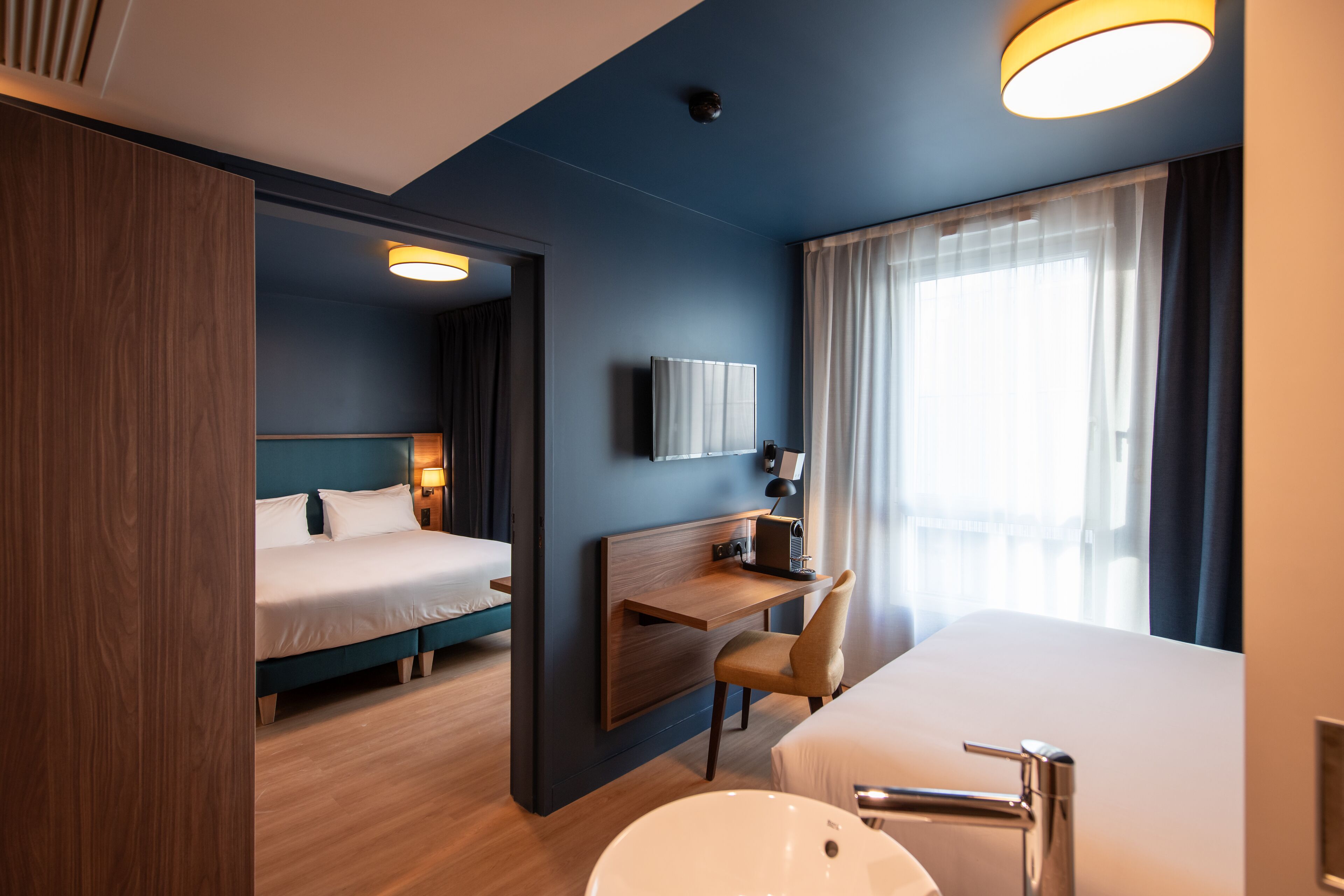 Ein modernes Hotelzimmer mit Bett, Schreibtisch, Stuhl und einem geräumigen Badezimmerwaschbecken.