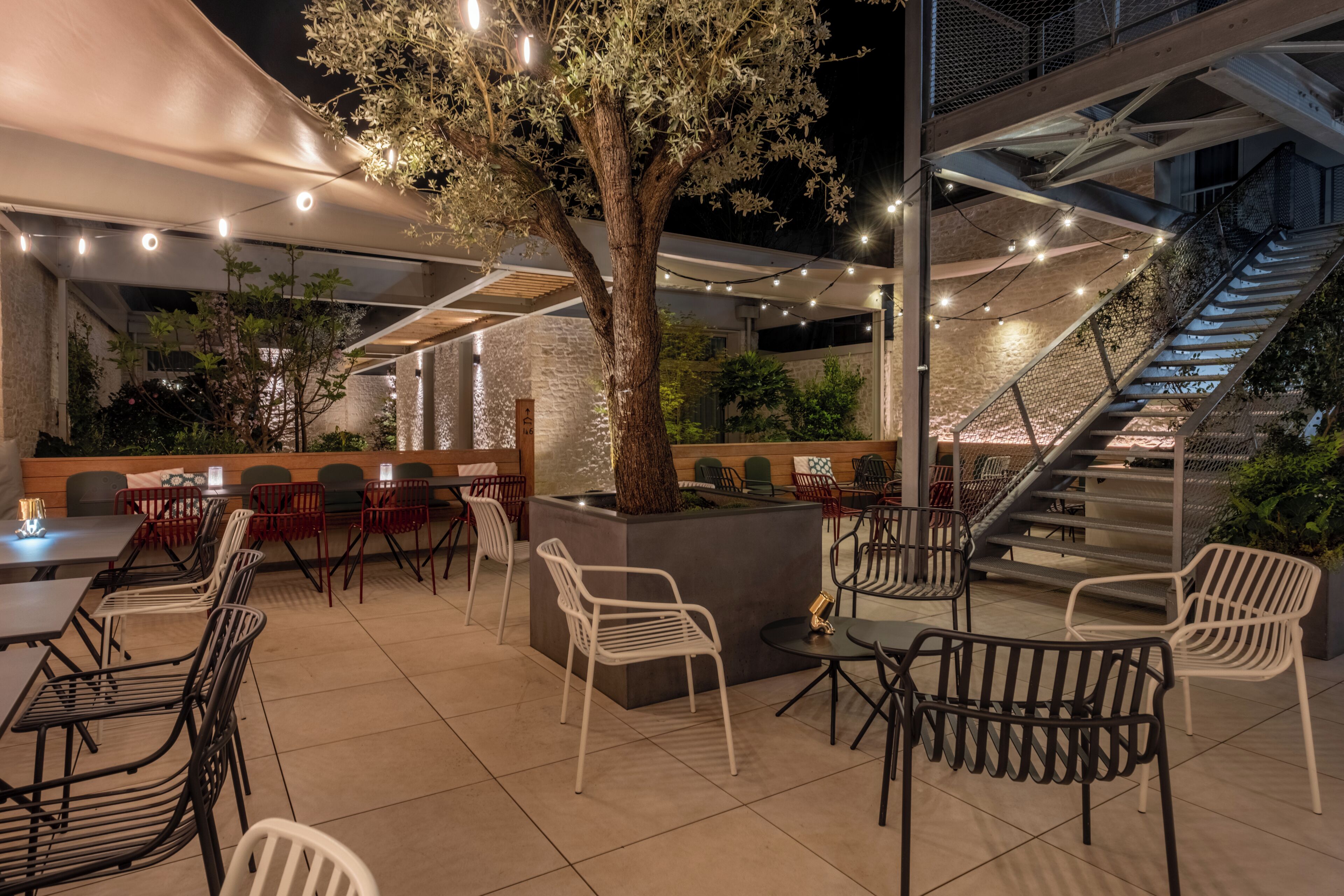 Un espace extérieur aménagé pour les repas, avec des tables et des chaises, un arbre et un escalier.