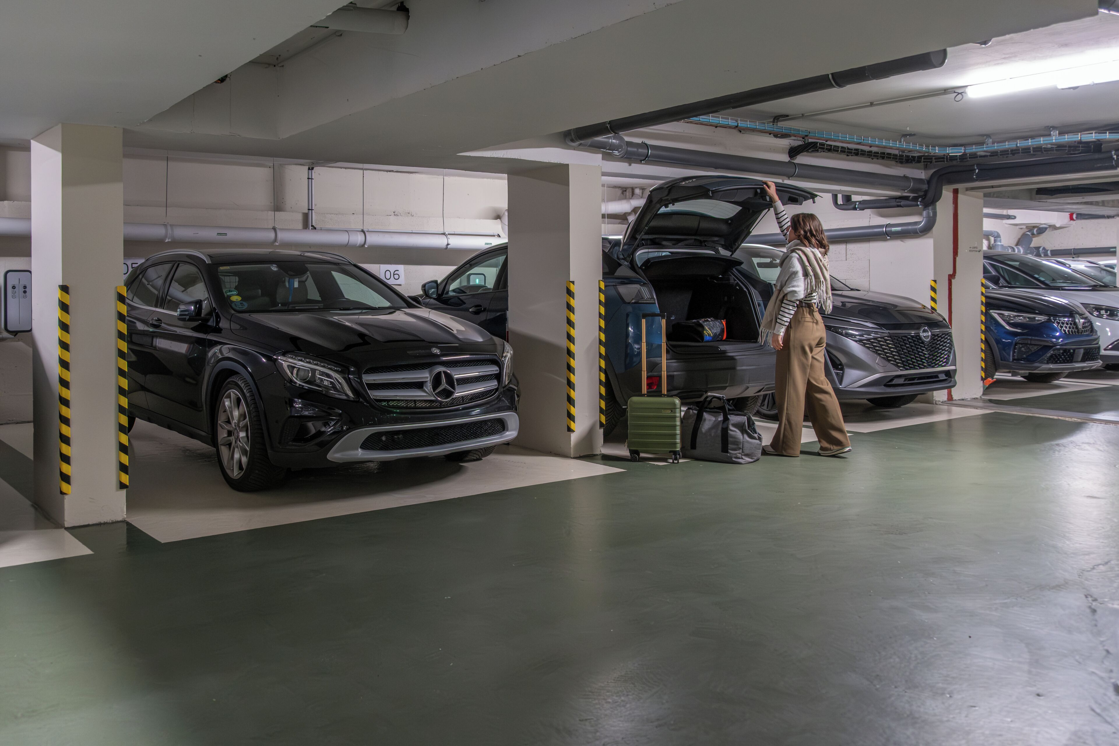 Un aparcamiento con varios coches, incluyendo un SUV Mercedes-Benz negro y un SUV plateado.