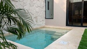 A rectangular pool with clear water, surrounded by a stone wall and a glass door leading to a room. - Quiet La Punta Surf Villa (Santa María Colotepec)