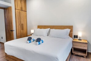 A neatly made bed with white linens, two pillows, and two rolled towels on the bed. There is a wooden headboard, a wooden nightstand with a lamp, and a wooden wardrobe with a door. - Quiet La Punta Surf Villa (Santa María Colotepec)